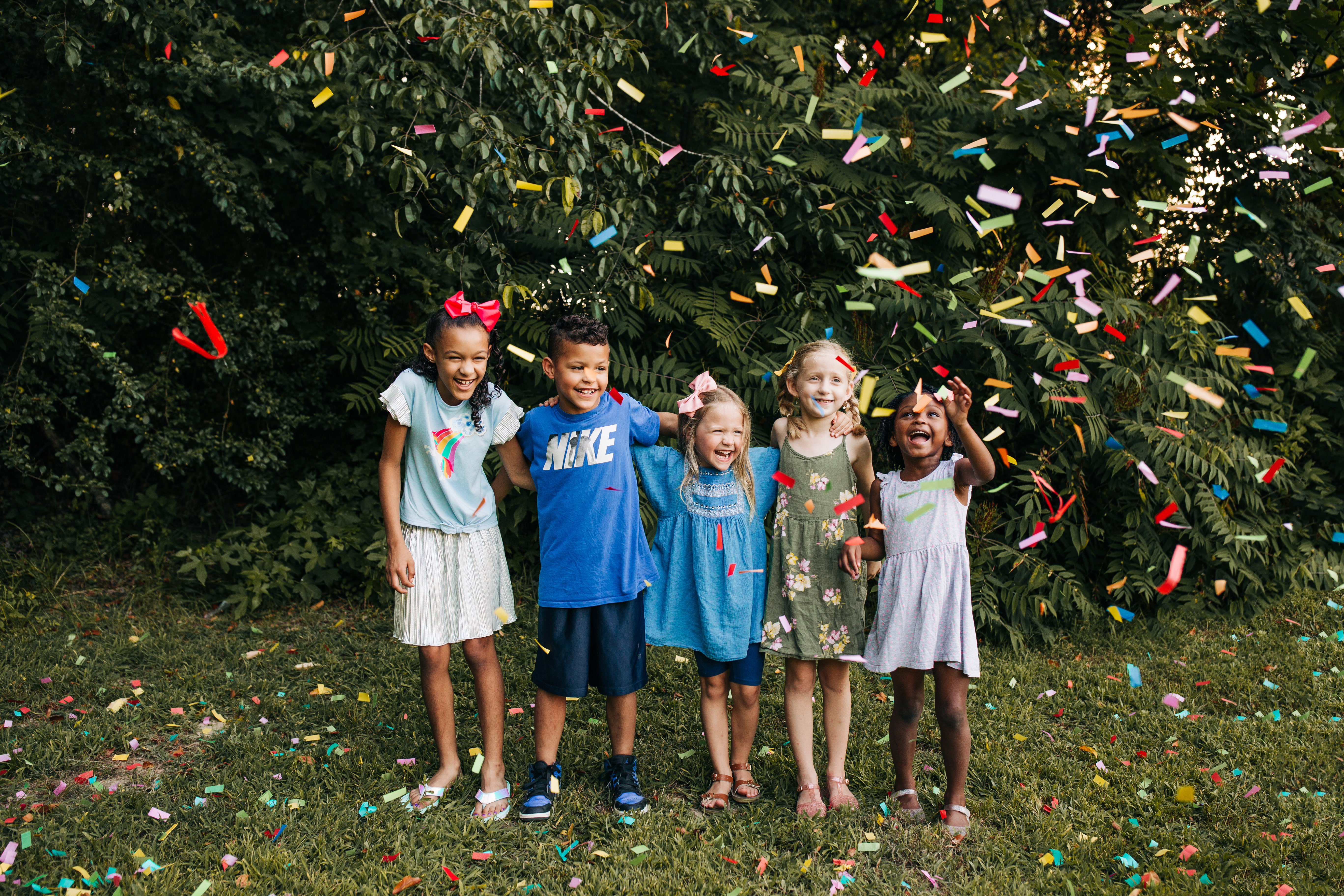Five children laughing together beneath colorful falling confetti.